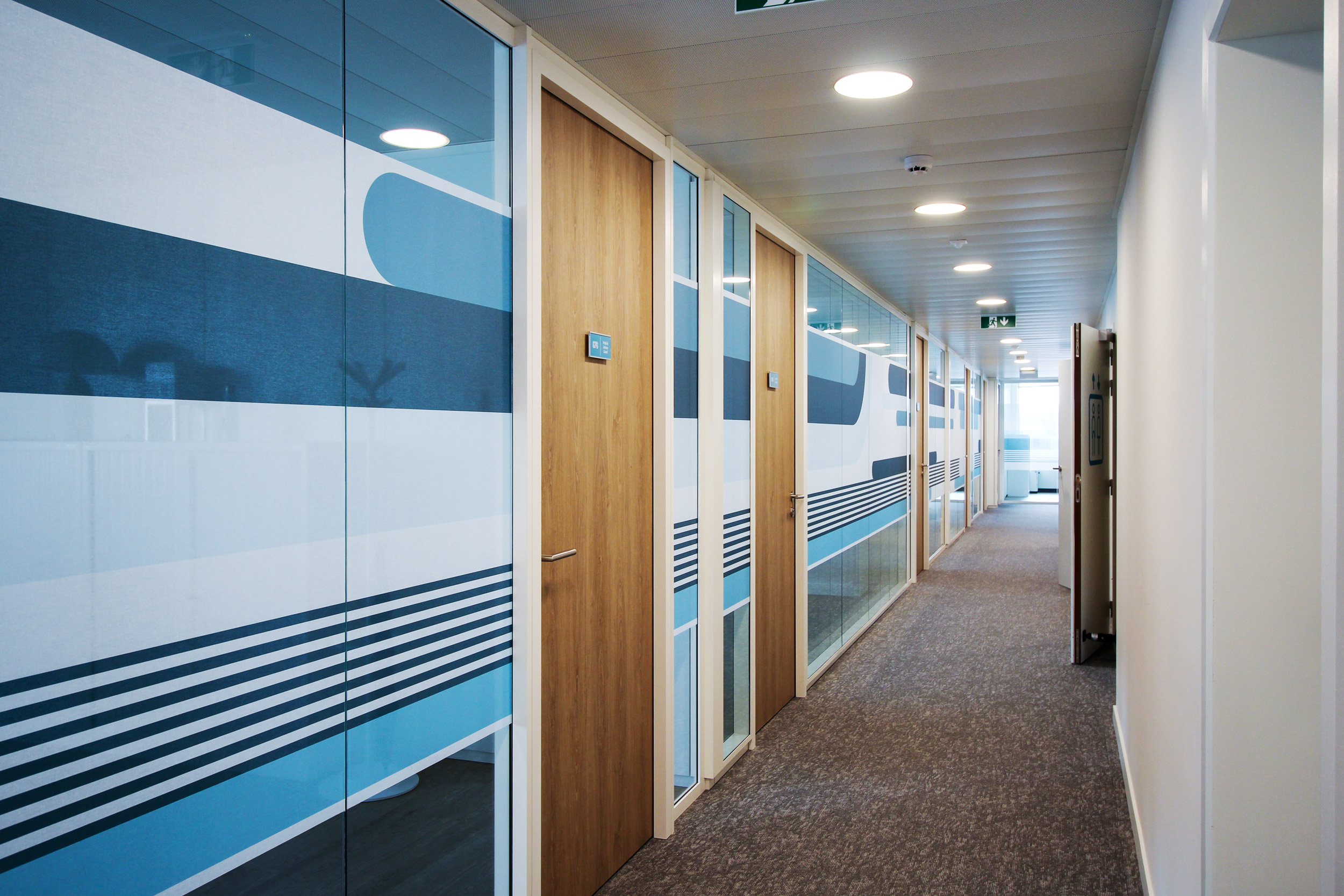 Vue d'ambiance d'un couloir avec plaques de port Skwizmi Marcal sur portes en bois et habillage décoratif sur cloisons vitrées en tissus autocollant design (Twodesigners) des bandes dans les tons de bleu