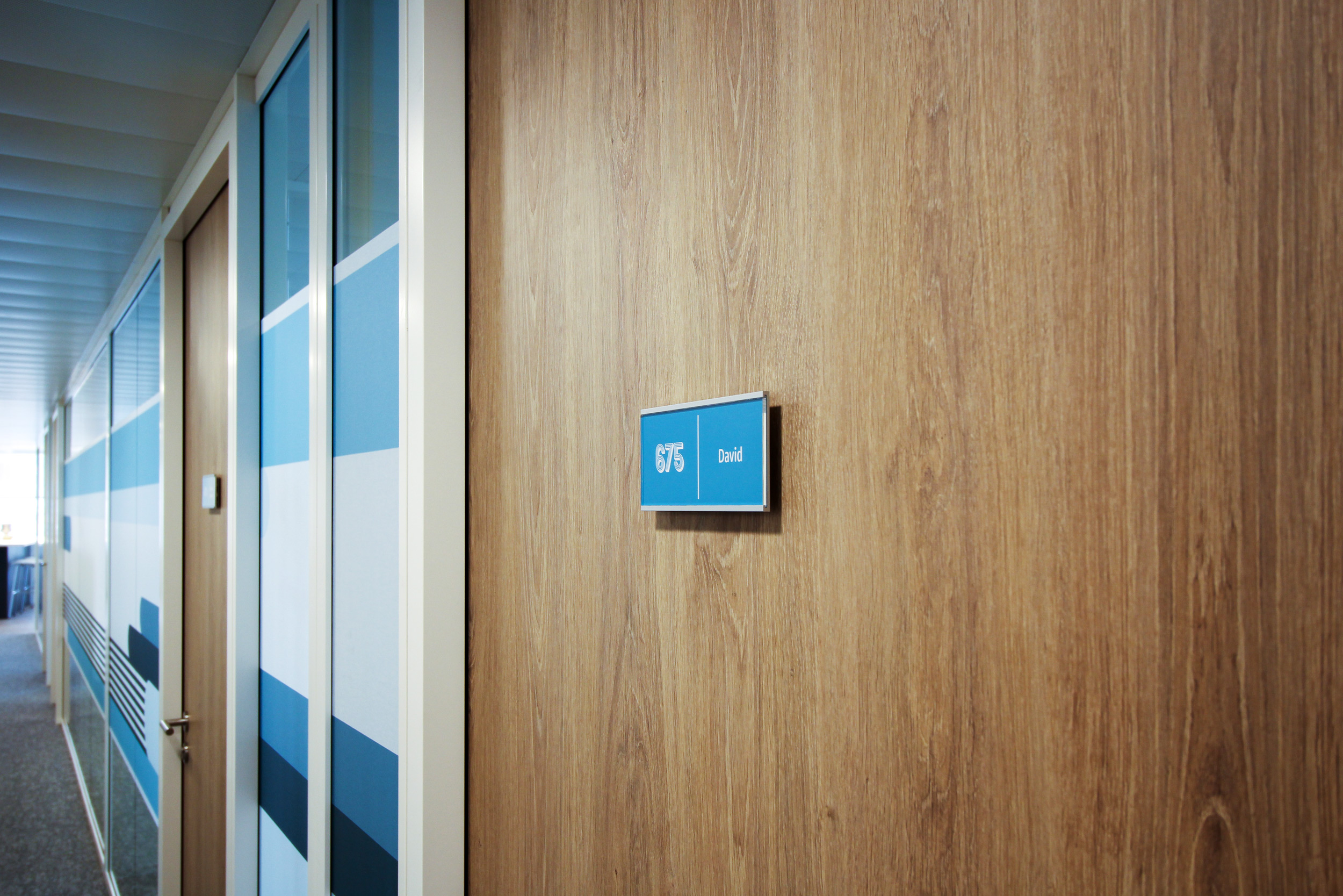 Zoom sur une plaque de porte Skwizmi de la gamme Marcal avec insert imprimé bleu sur une porte en bois