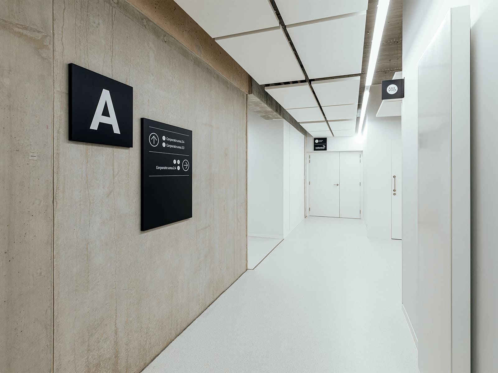 Vue d'un couloir du Legiapark avec la mise en évidence de plusieurs éléments de signalétique: une balise directionnelle, un drapeau pour indiquer les toilettes et une box entreprise pour identifier l'entreprise qui loue cet espace.